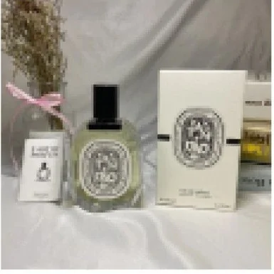 Frasco de perfume transparente con etiqueta ovalada junto a su caja blanca y una ramita seca