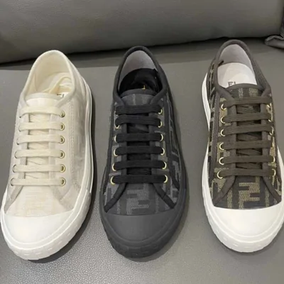 Tres zapatillas de lona de caña baja con cordones, en blanco, negro y gris estampado, sobre un sofá